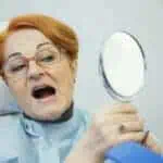 woman looks at teeth in mirror